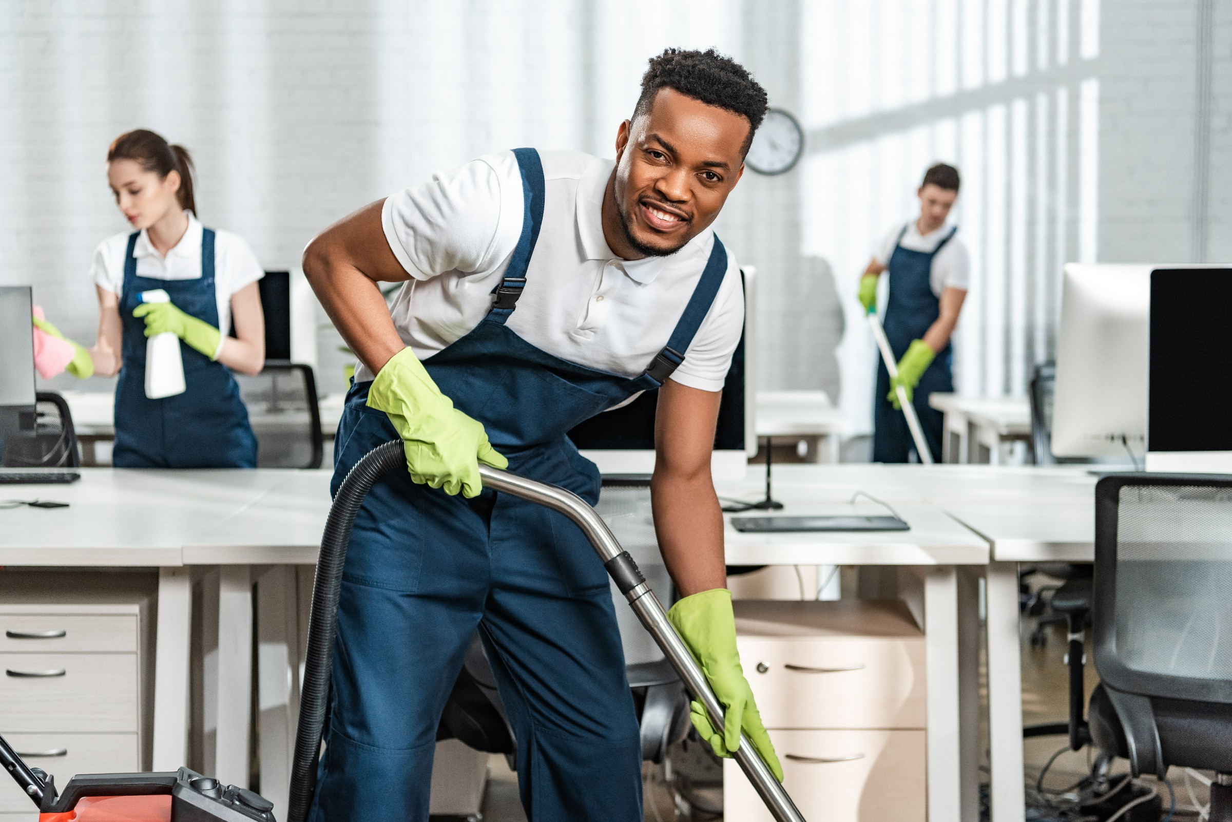 cheerful african american cleaner vacuuming floor while looking at camera